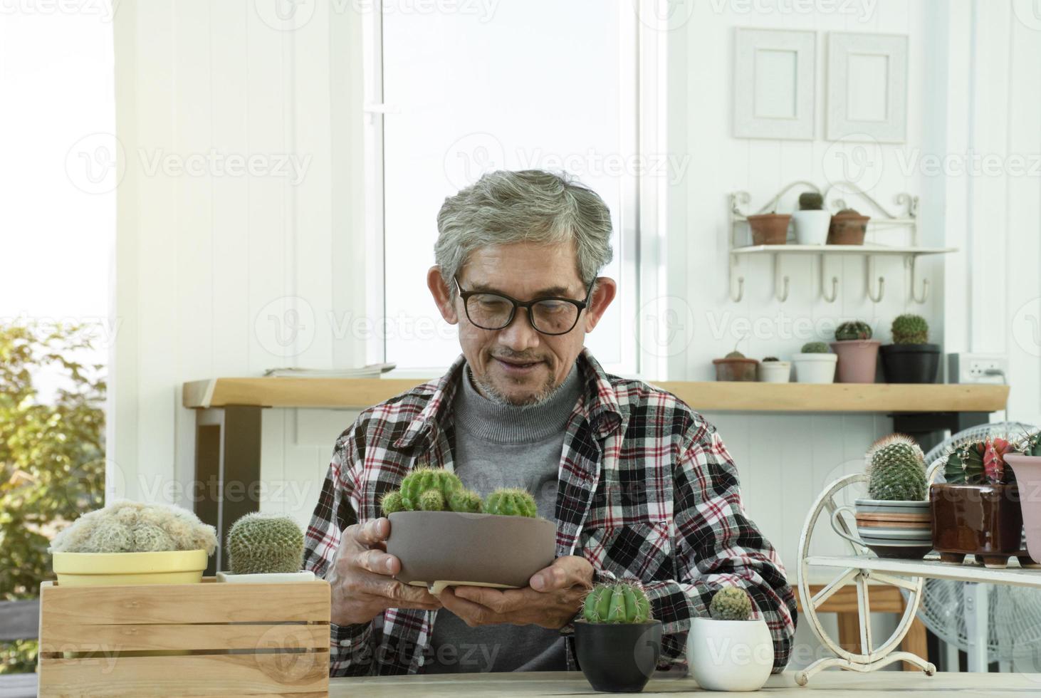 Portrait d'un homme asiatique senior âgé assis près d'une fenêtre en verre le matin pour travailler à domicile et vérifier ses affaires sur son ordinateur portable sur la table avec une mise au point sérieuse, douce et sélective. photo