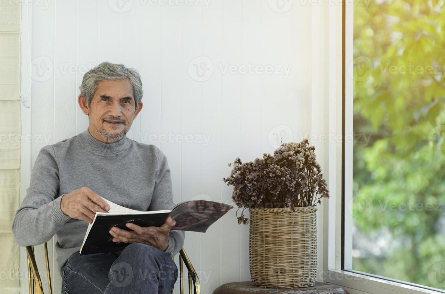 Portrait d'un homme asiatique senior âgé assis près d'une fenêtre en verre le matin pour travailler à domicile et vérifier ses affaires sur son ordinateur portable sur la table avec une mise au point sérieuse, douce et sélective. photo