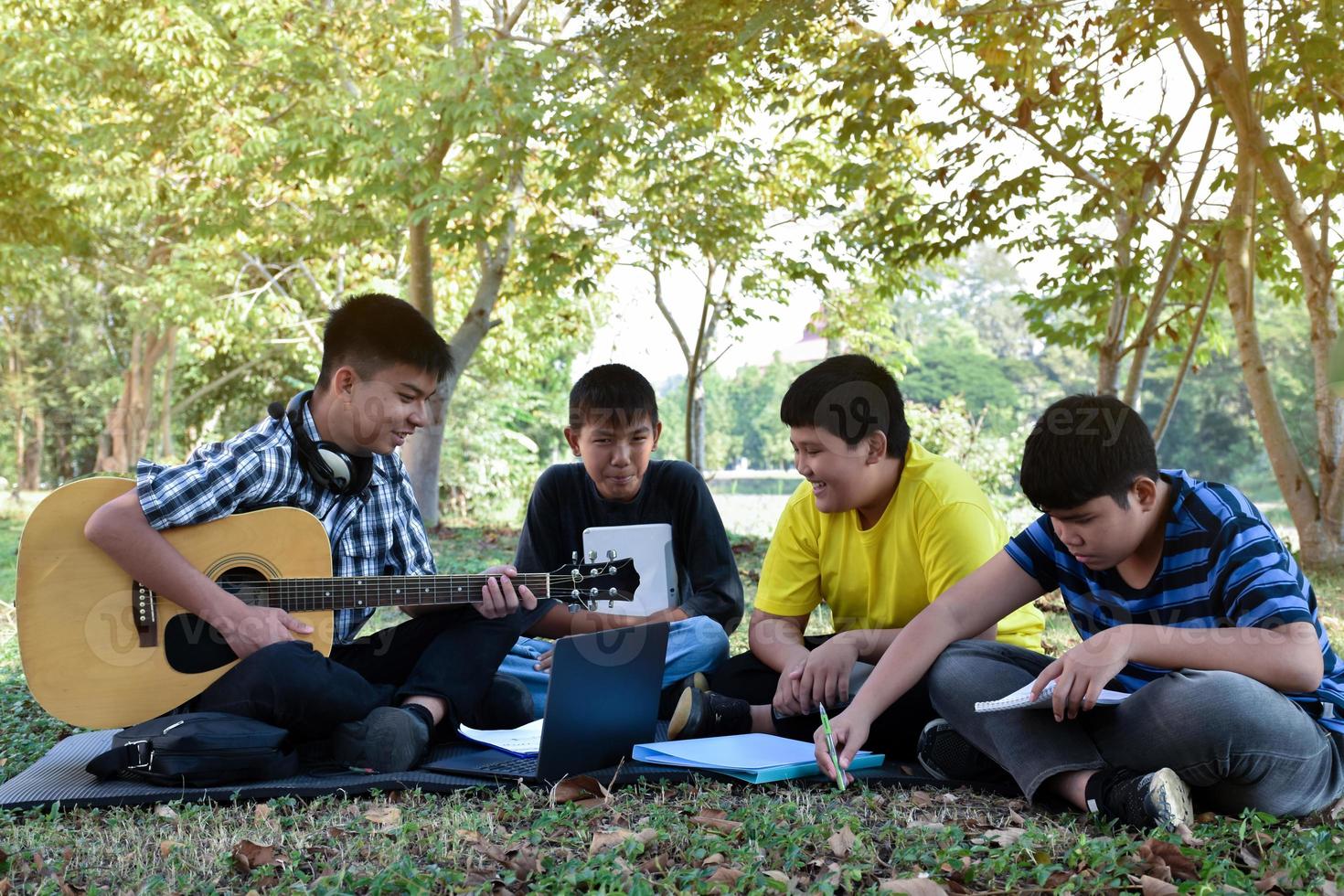 jeunes adolescents asiatiques assis ensemble, parlant, lisant, consultant et jouant du quitar le week-end dans le parc, mise au point douce et sélective. photo