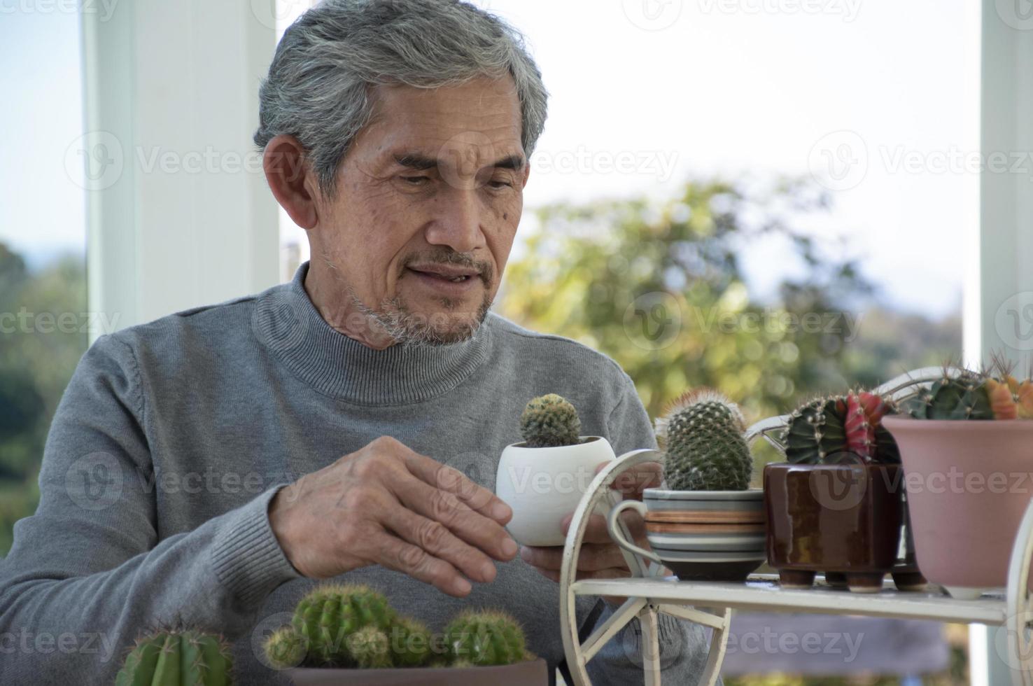 Portrait d'un homme asiatique senior âgé assis près d'une fenêtre en verre le matin pour travailler à domicile et vérifier ses affaires sur son ordinateur portable sur la table avec une mise au point sérieuse, douce et sélective. photo