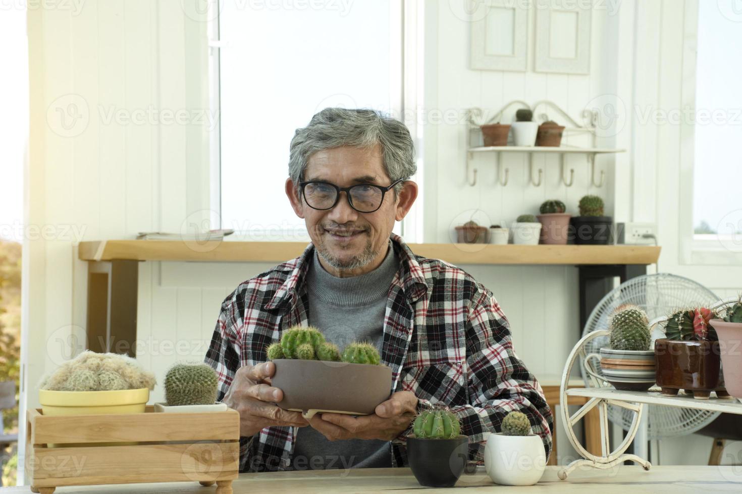 Portrait d'un homme asiatique senior âgé assis près d'une fenêtre en verre le matin pour travailler à domicile et vérifier ses affaires sur son ordinateur portable sur la table avec une mise au point sérieuse, douce et sélective. photo