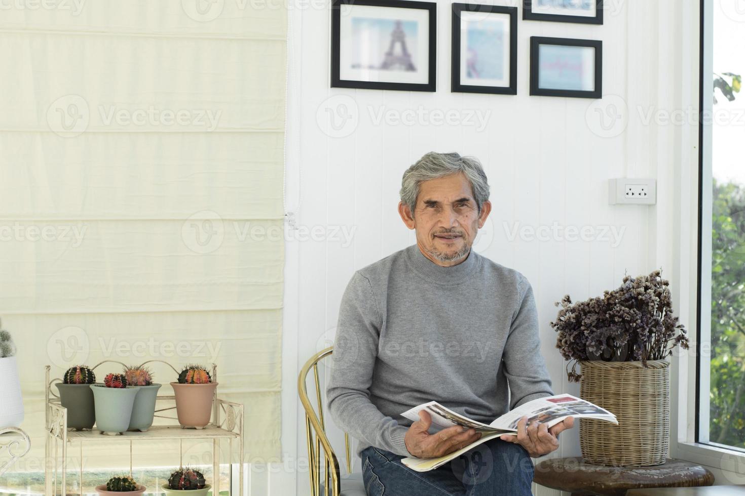 Portrait d'un homme asiatique senior âgé assis près d'une fenêtre en verre le matin pour travailler à domicile et vérifier ses affaires sur son ordinateur portable sur la table avec une mise au point sérieuse, douce et sélective. photo