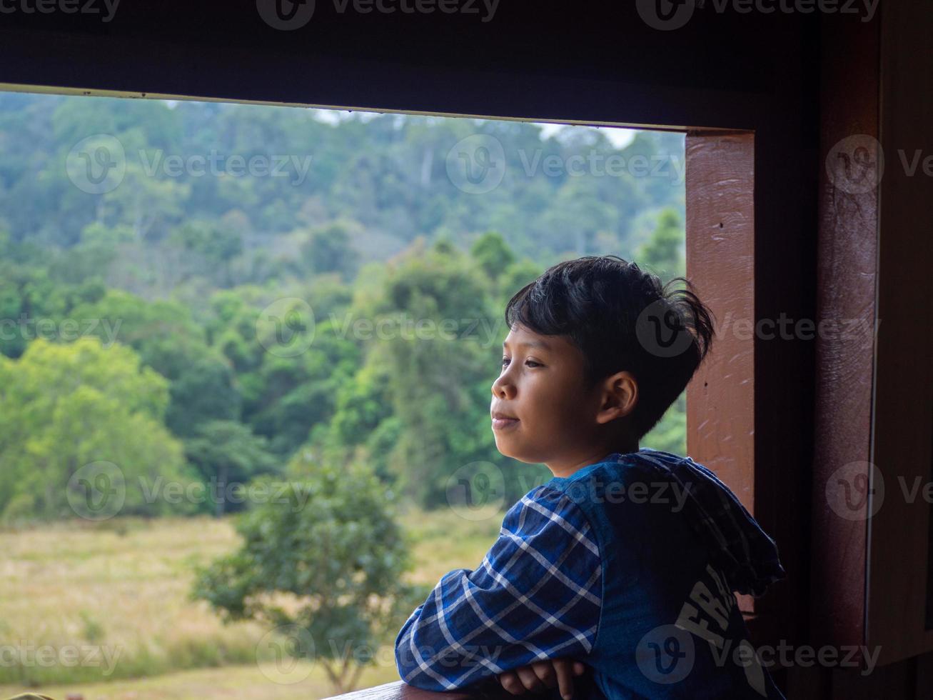 garçon regardant par la fenêtre en regardant la forêt verte photo