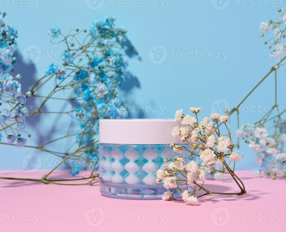 pot en verre transparent avec crème pour le visage sur fond bleu rose, cosmétiques photo