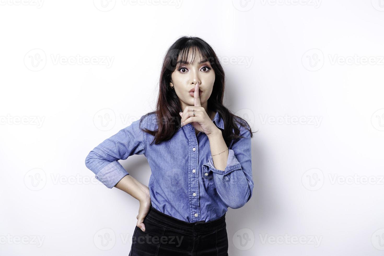 portrait d'une jeune femme asiatique dites être tranquille, chut avec un visage sérieux, chut avec le doigt appuyé sur les lèvres, isolé par fond blanc photo