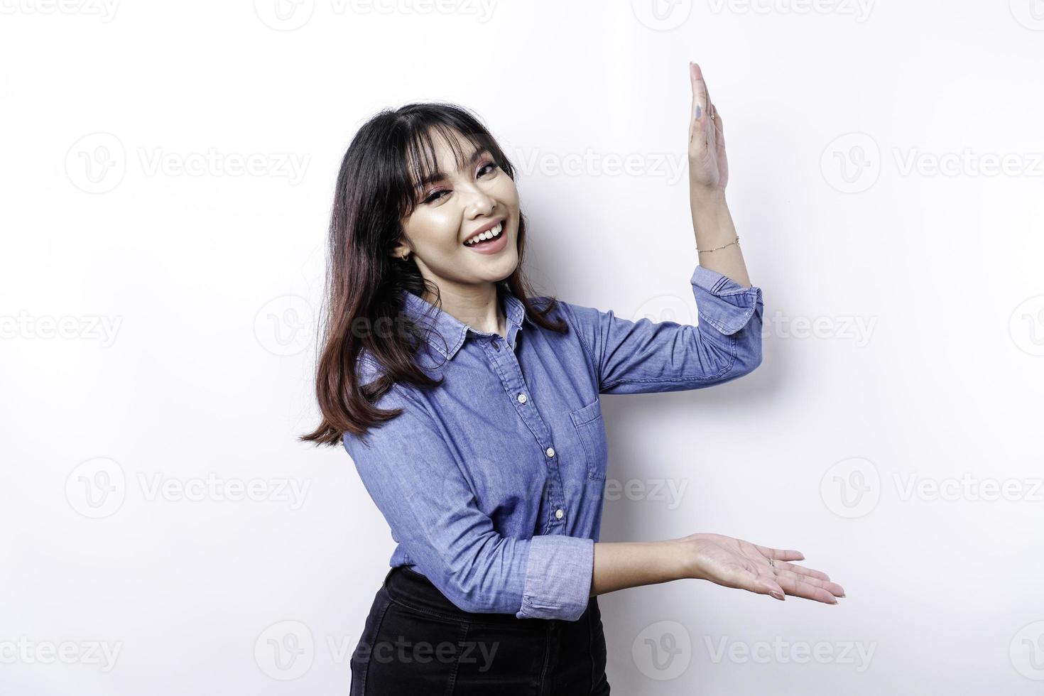 femme asiatique excitée portant une chemise bleue pointant vers l'espace de copie à côté d'elle, isolée par fond blanc photo