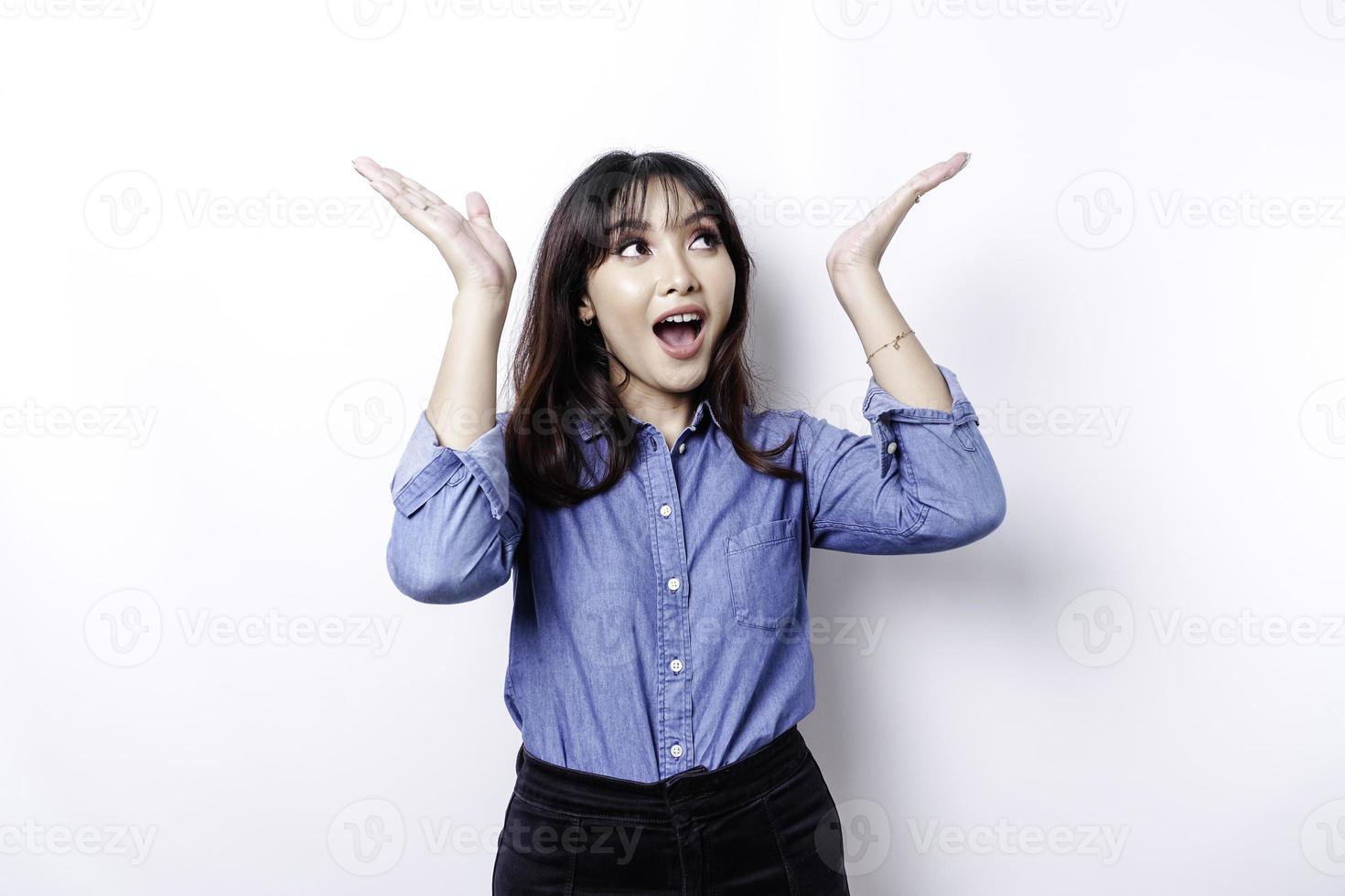 femme asiatique choquée portant une chemise bleue pointant vers l'espace de copie au-dessus d'elle, isolée par fond blanc photo