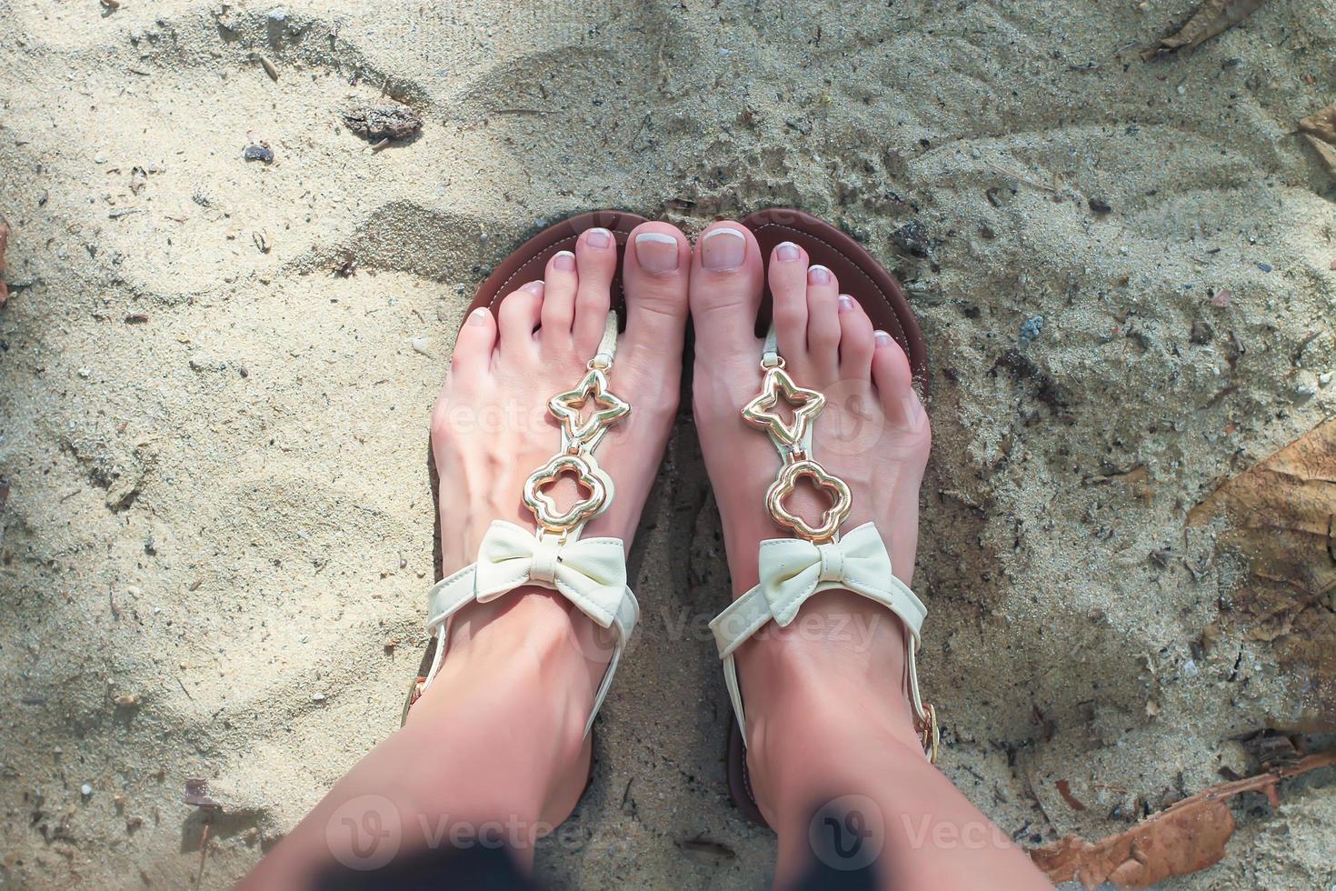 gros plan de tongs lumineuses et de jambes sur du sable blanc photo