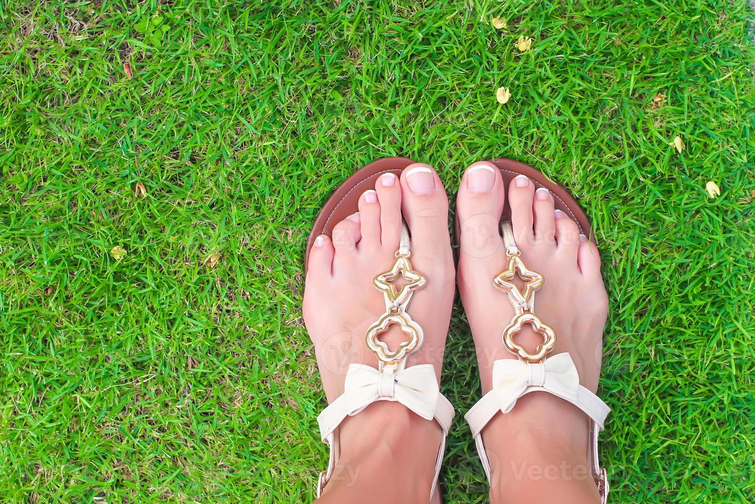 gros plan de tongs lumineuses et de jambes sur l'herbe verte photo