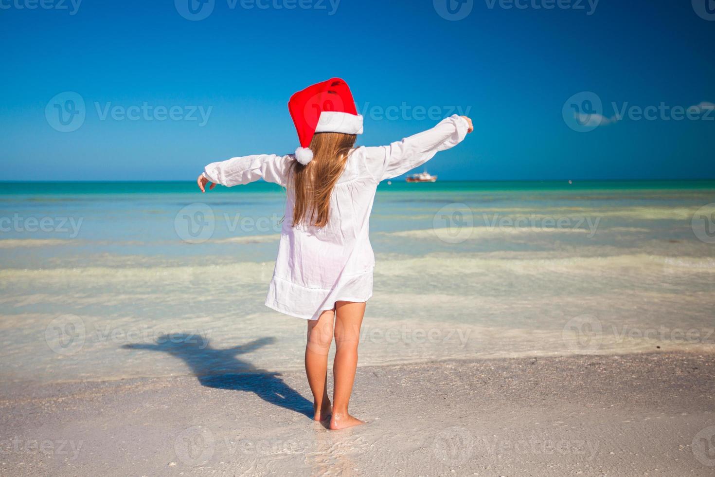 vue arrière de la petite fille mignonne au chapeau rouge le père noël sur la plage photo