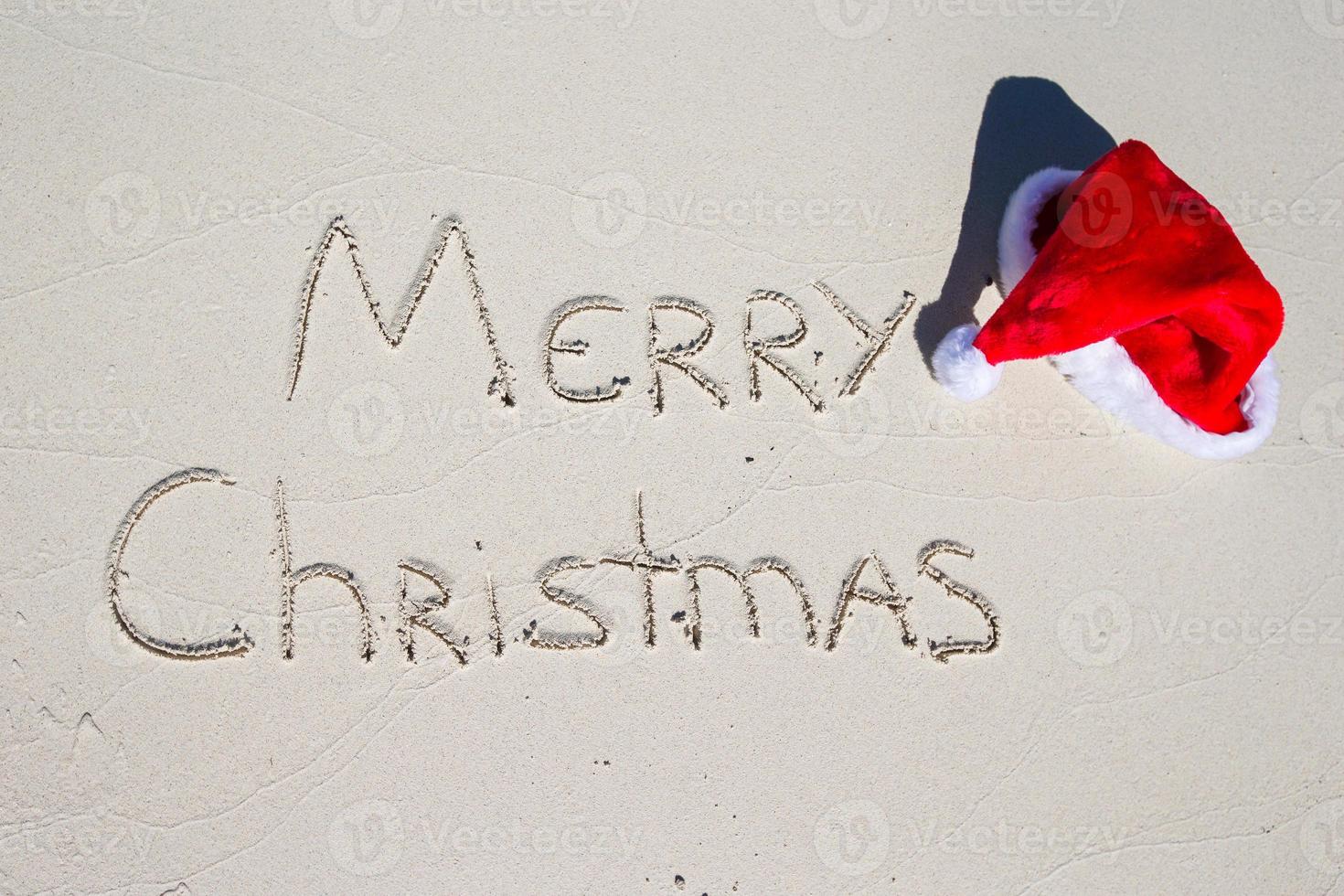 Joyeux Noël écrit sur le sable blanc de la plage tropicale avec un chapeau de Noël photo