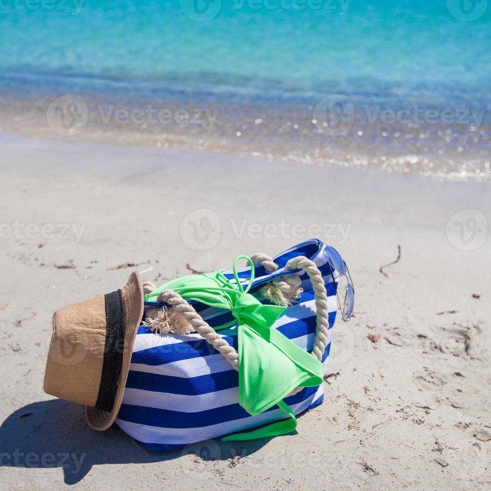 sac à rayures, chapeau de paille, crème solaire et frisbee sur une plage tropicale de sable blanc photo