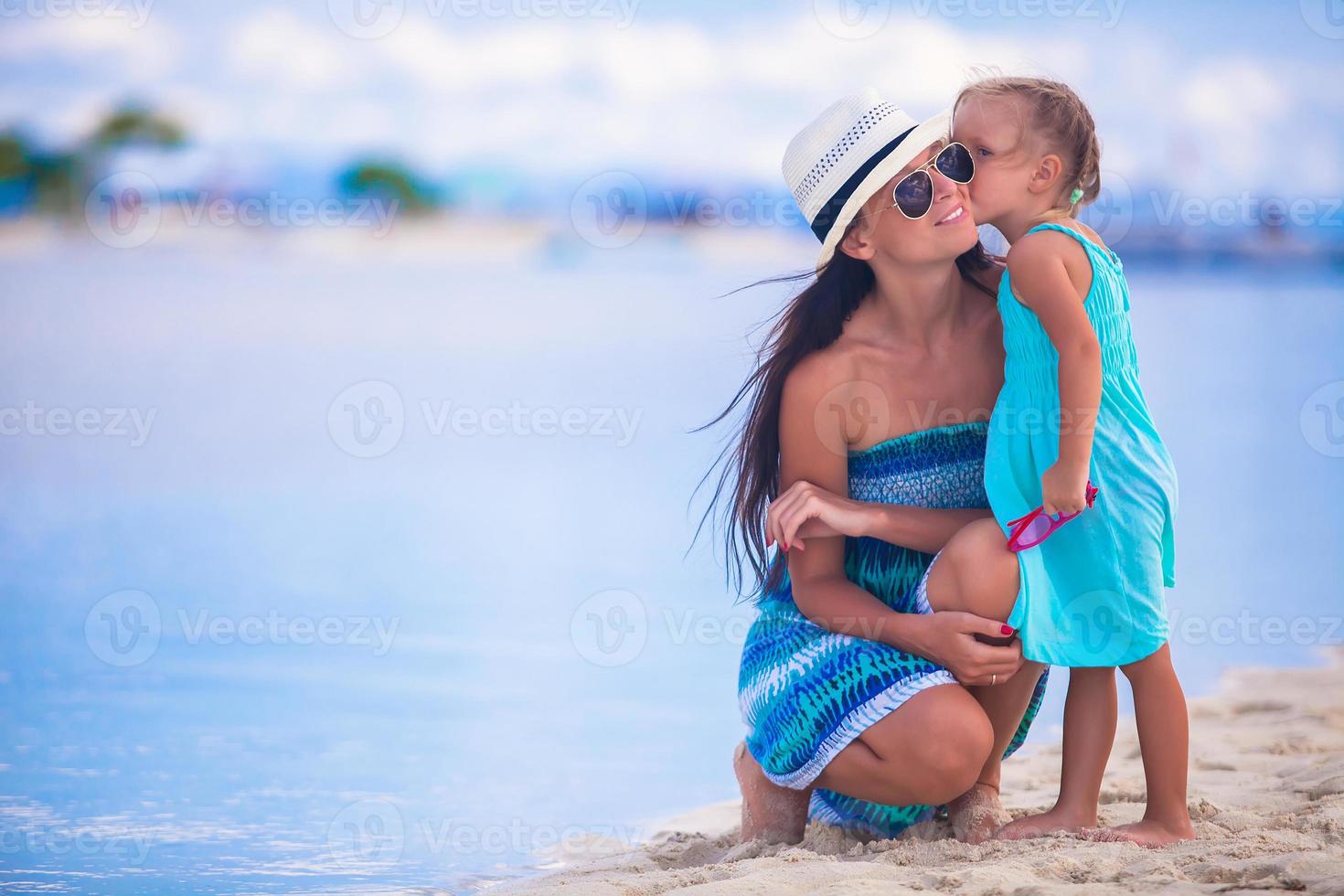 petite fille embrassant sa mère sur une plage tropicale blanche photo