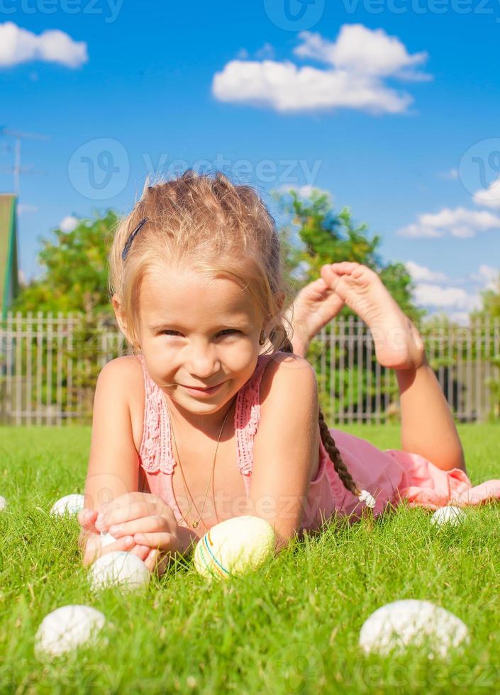 portrait de petite fille heureuse jouant avec des oeufs de pâques blancs sur l'herbe verte photo