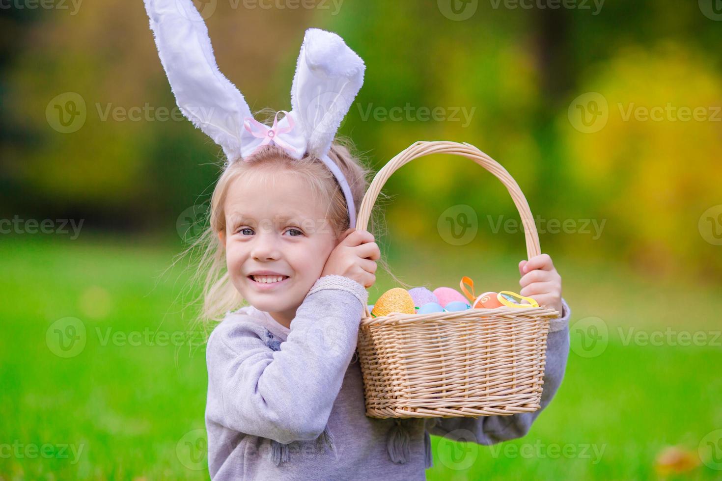 heureuse petite fille portant des oreilles de lapin avec un panier rempli d'oeufs de pâques le jour du printemps à l'extérieur photo