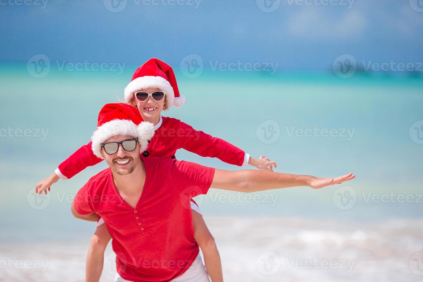 petite fille et père heureux en bonnet de noel pendant les vacances de noël à la plage photo