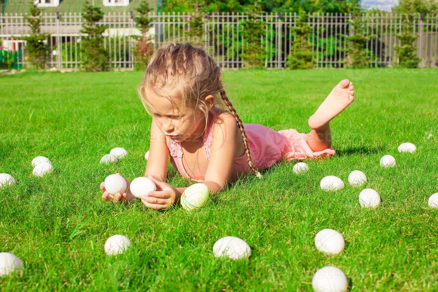 petite fille heureuse jouant avec des oeufs de pâques blancs sur l'herbe verte photo