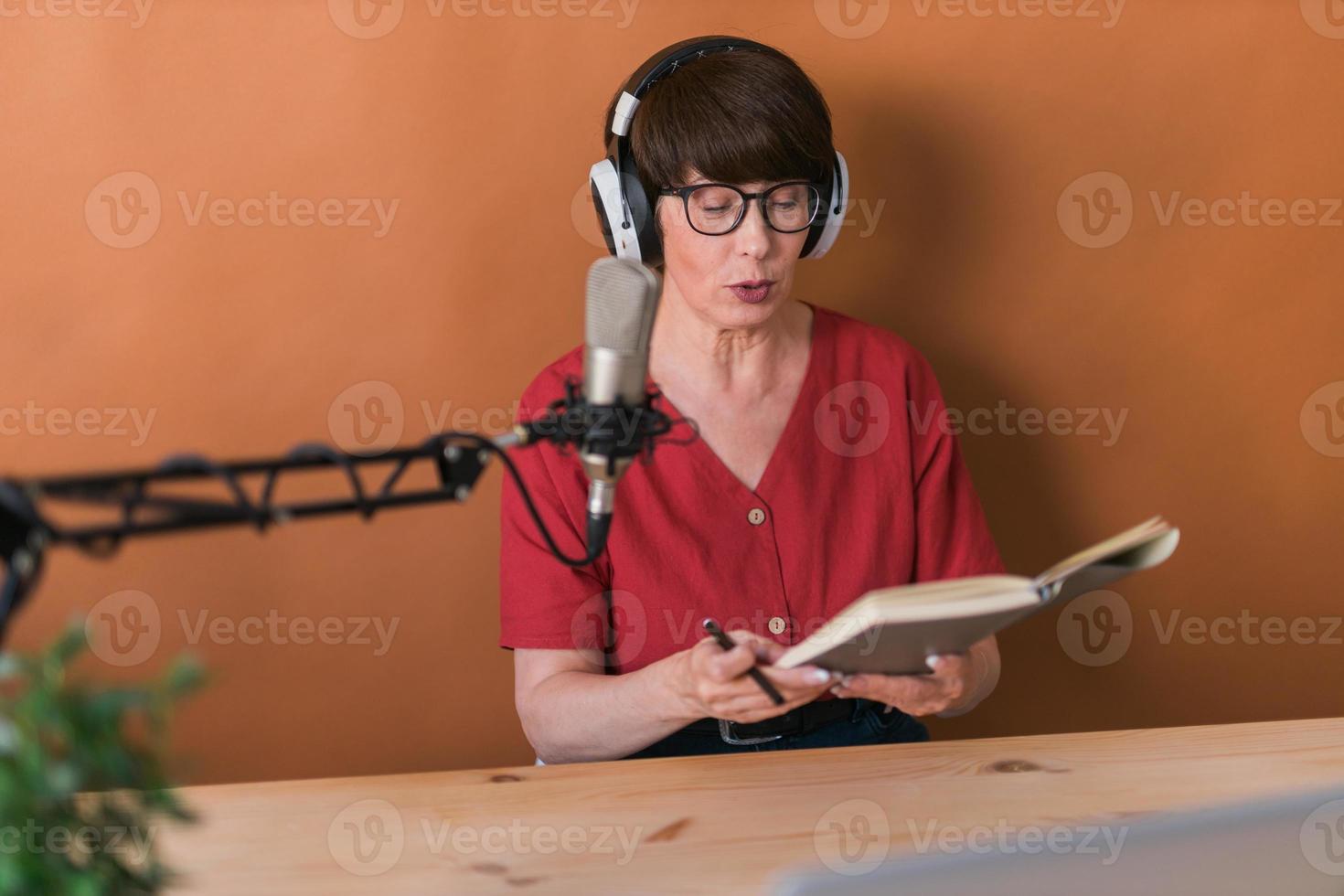 femme mûre faisant un enregistrement de podcast pour son émission en ligne. Jolie femme d'affaires à l'aide d'écouteurs devant le microphone pour une émission de radio photo