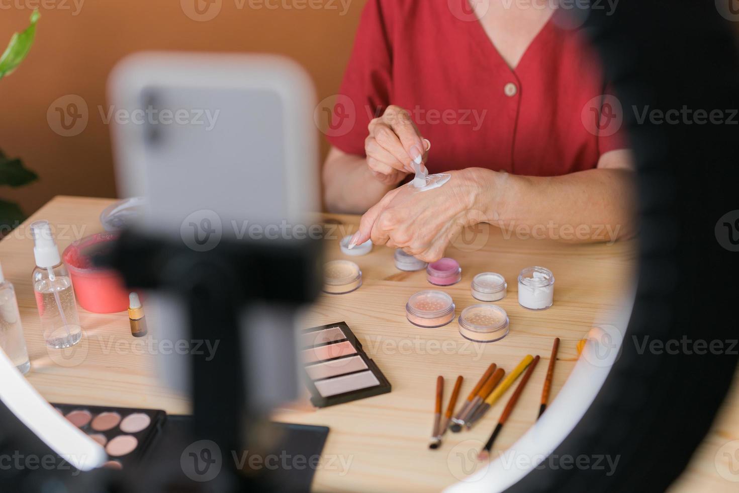 femme d'âge moyen parlant de cosmétiques avec des ombres à paupières de maquillage et une palette de blush et des pinceaux tout en enregistrant sa vidéo. femme mûre réalisant une vidéo pour son blog sur les cosmétiques photo