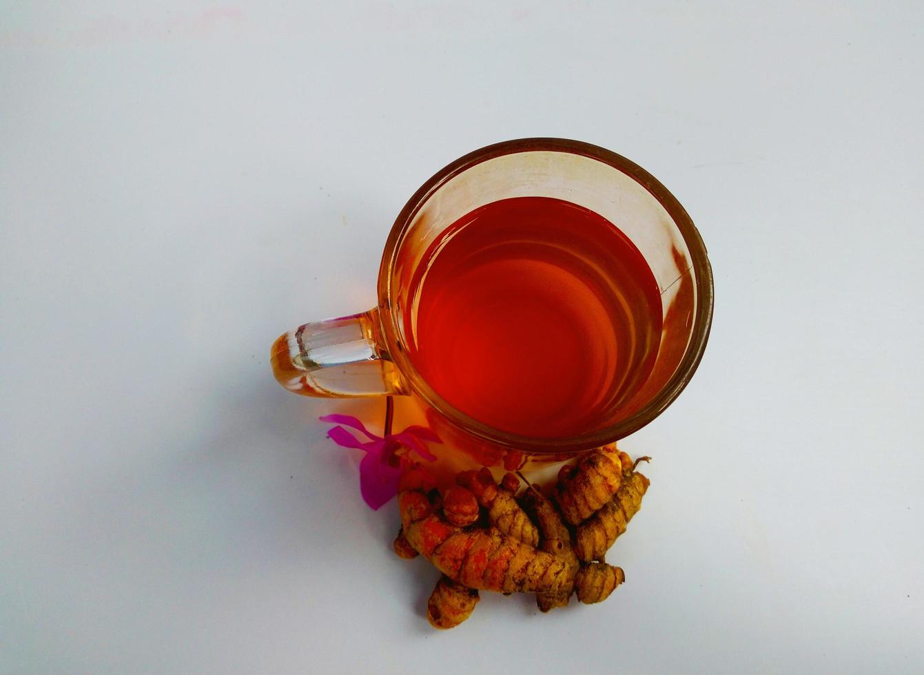 gros plan de morceaux de curcuma sur une nappe décorée, boisson jamu indonésienne traditionnelle dans une bouteille et dans une tasse. photo