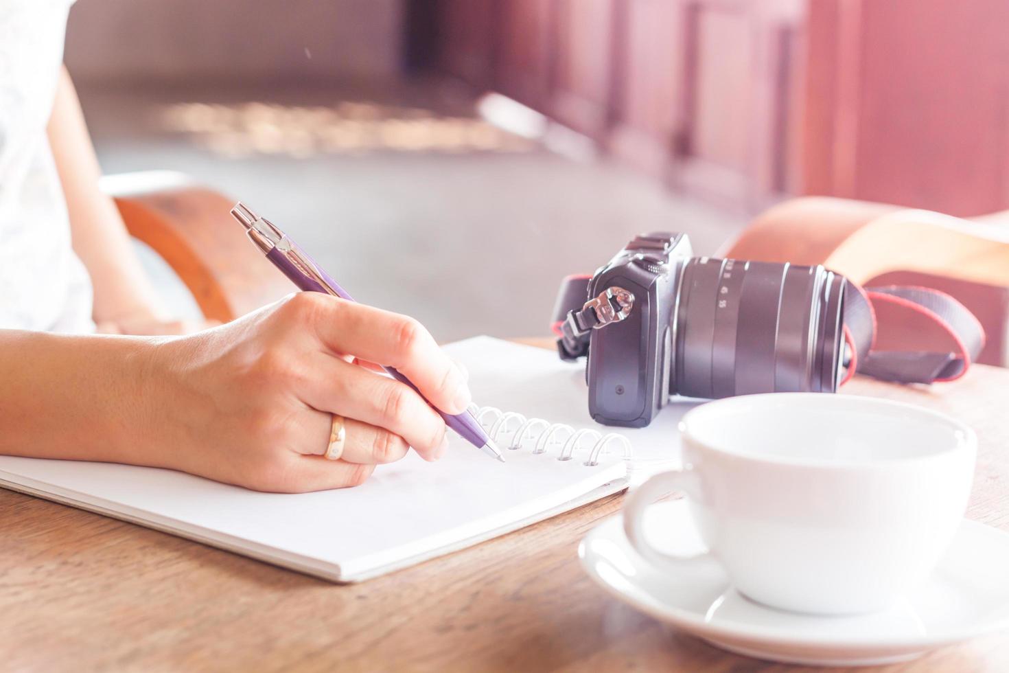 Femme écrivant dans un ordinateur portable avec un appareil photo et du café sur une table