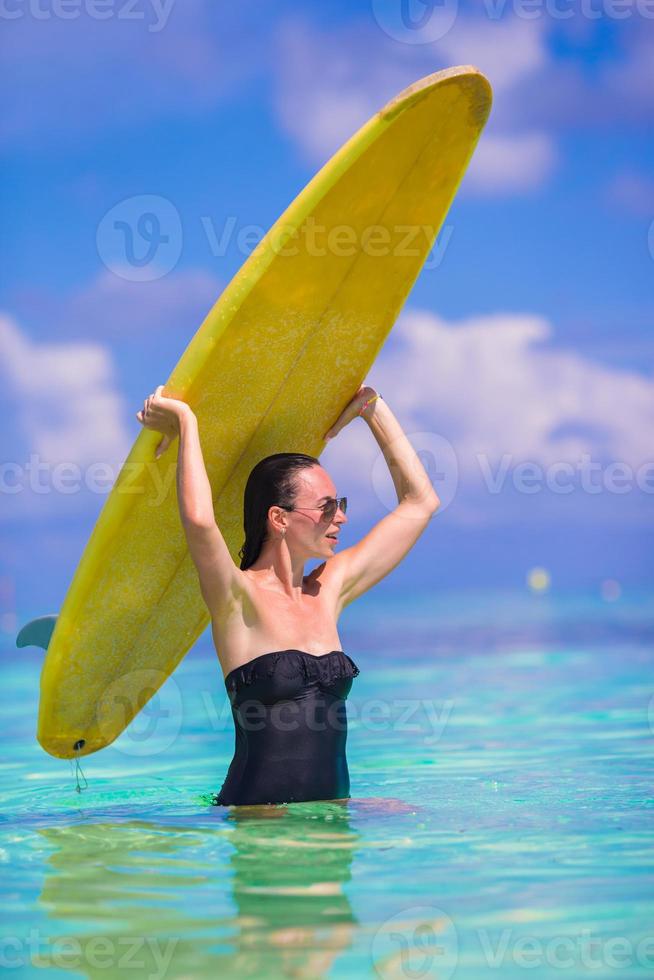 femme de surf bien faite heureuse à la plage blanche avec une planche de surf jaune photo