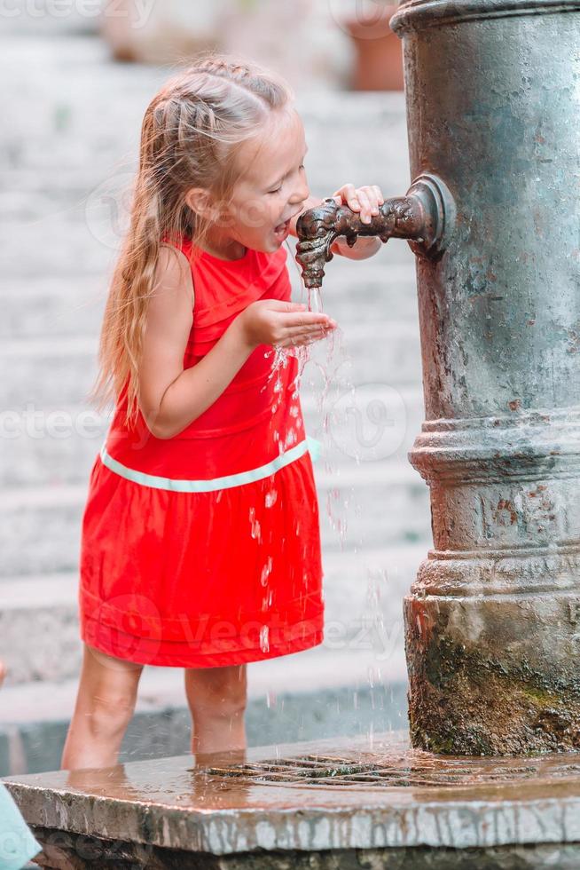 petite fille s'amusant avec de l'eau potable à la fontaine de la rue à rome, italie photo