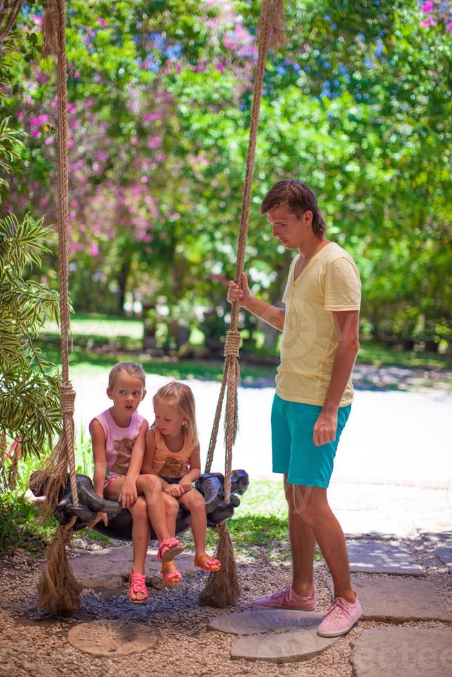 papa secoue ses jeunes filles sur une balançoire dans un hôtel tropical photo