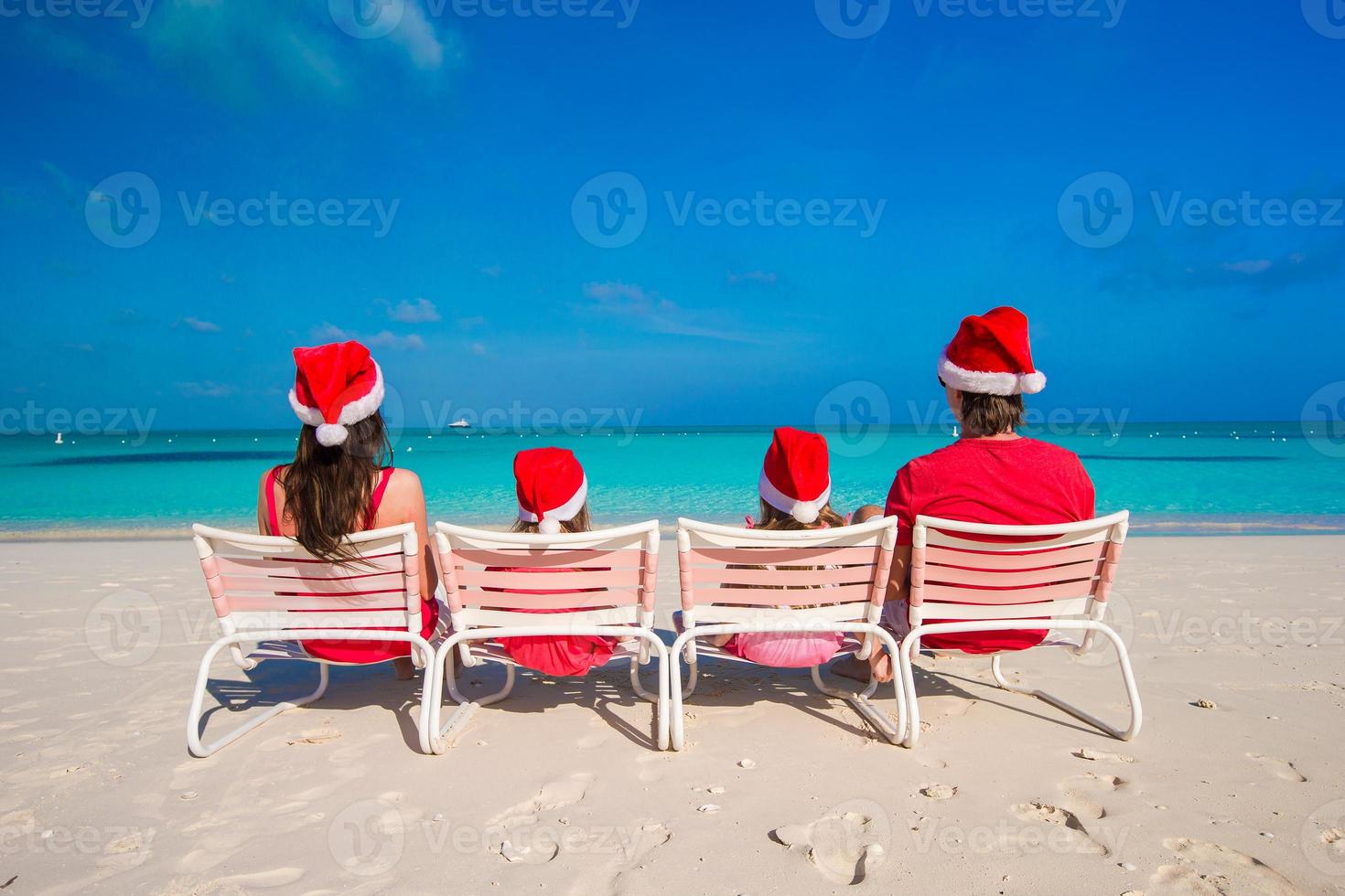 famille heureuse de quatre personnes sur la plage en chapeaux rouges de santa photo