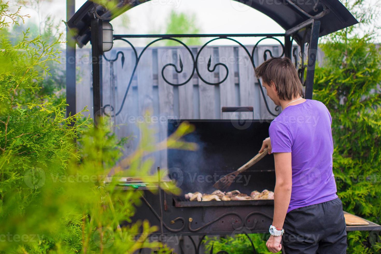 jeune homme fait frire des steaks sur le grill en plein air dans sa cour photo