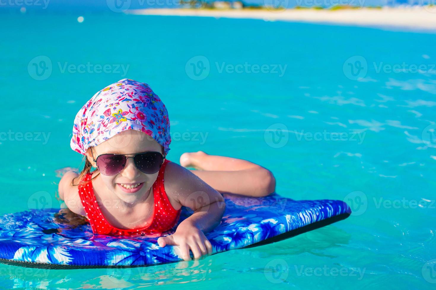 petite fille adorable sur une planche de surf dans la mer turquoise photo