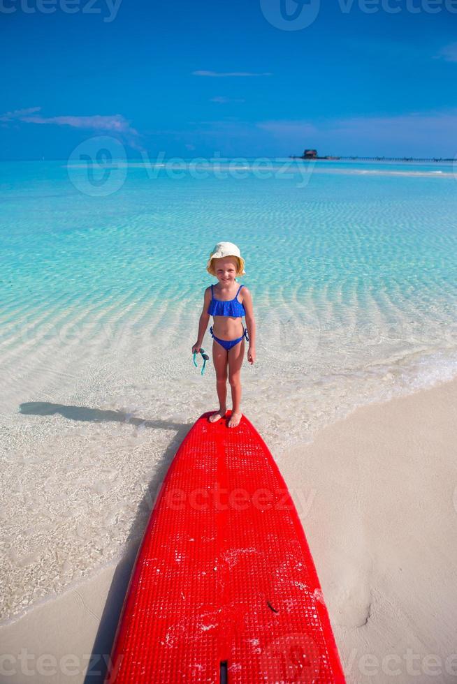 petite fille adorable sur une planche de surf dans la mer turquoise photo