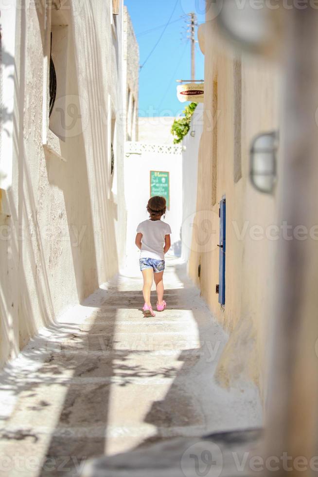 vue arrière de l'adorable fille marchant seule dans les rues étroites du village d'emporio sur l'île de santorin, grèce photo