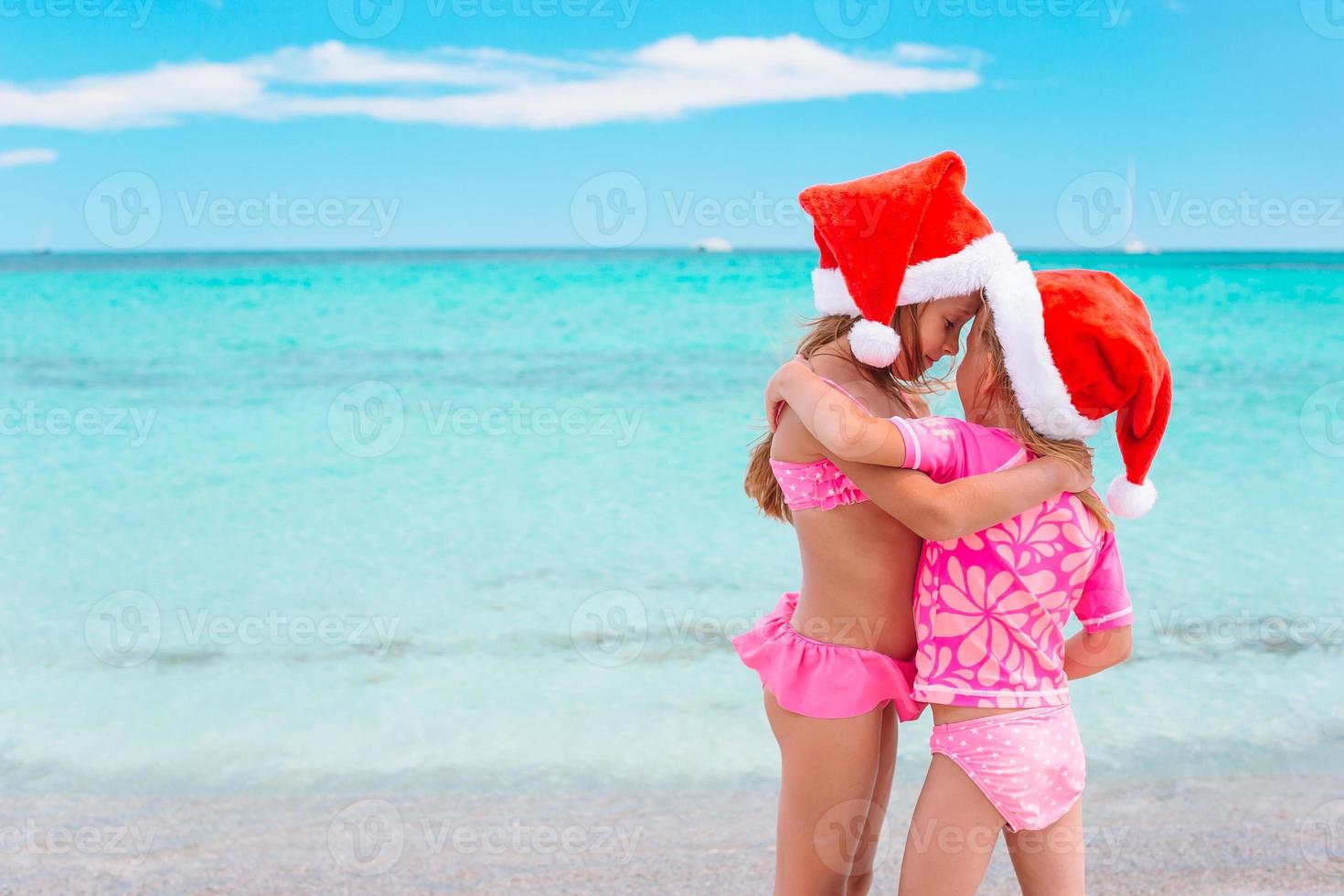 petites filles adorables en chapeaux de père noël pendant les vacances à la plage s'amuser ensemble photo
