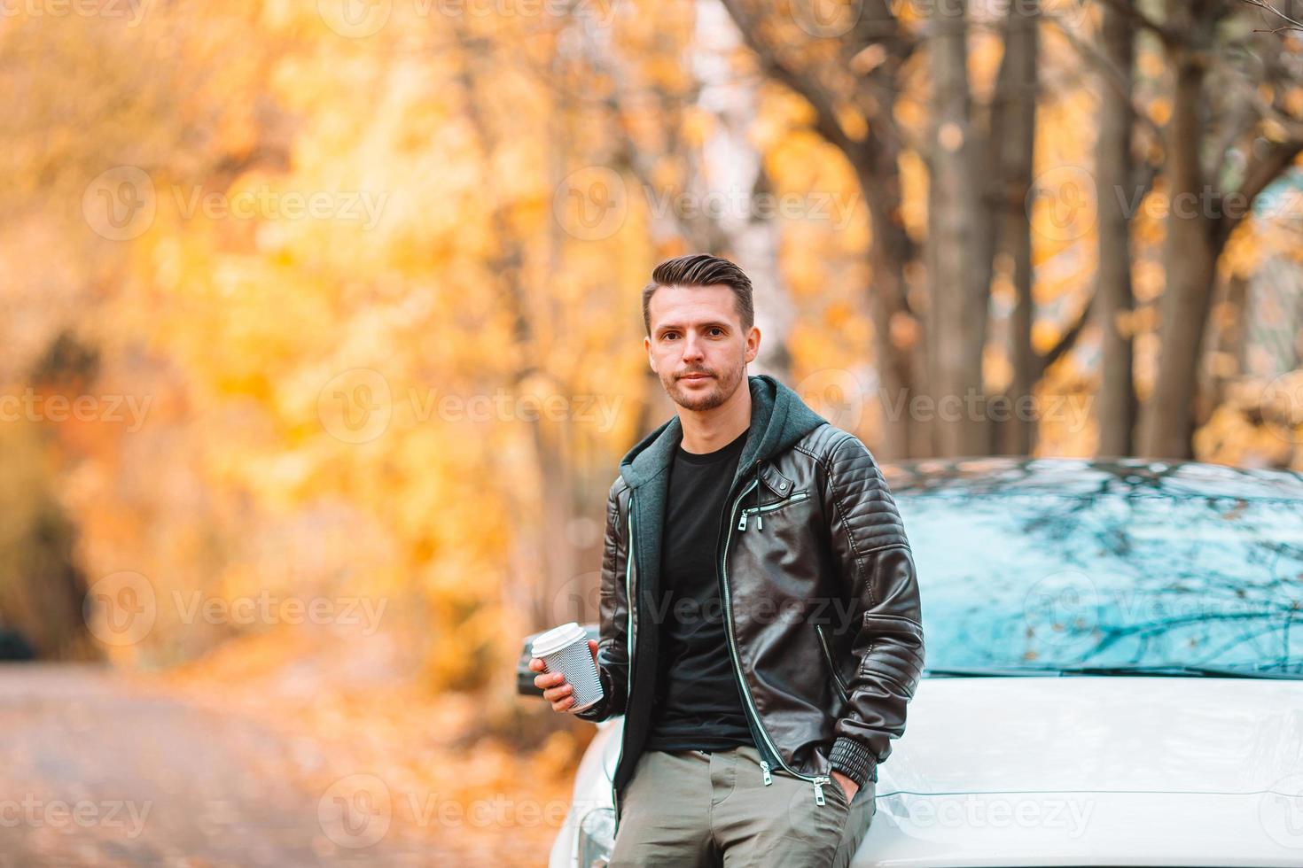jeune homme buvant du café avec téléphone dans le parc d'automne à l'extérieur photo
