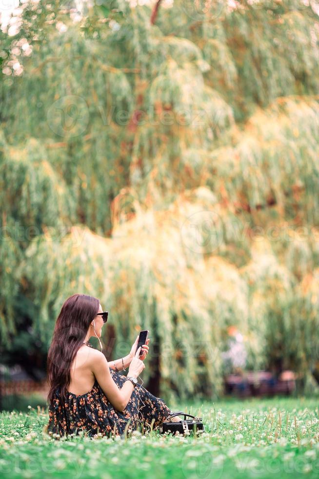 jolie femme lit un message texte sur son téléphone portable alors qu'elle est assise dans le parc. photo