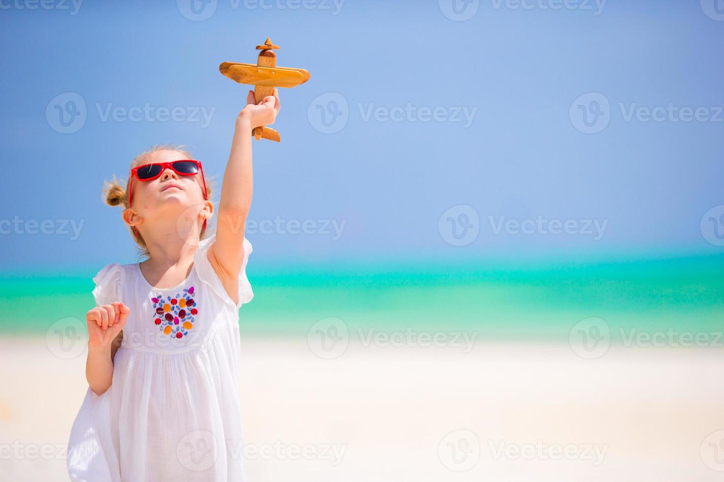 bonne petite fille avec un avion jouet dans les mains sur la plage de sable blanc. publicité photo de voyage, vols et compagnies aériennes