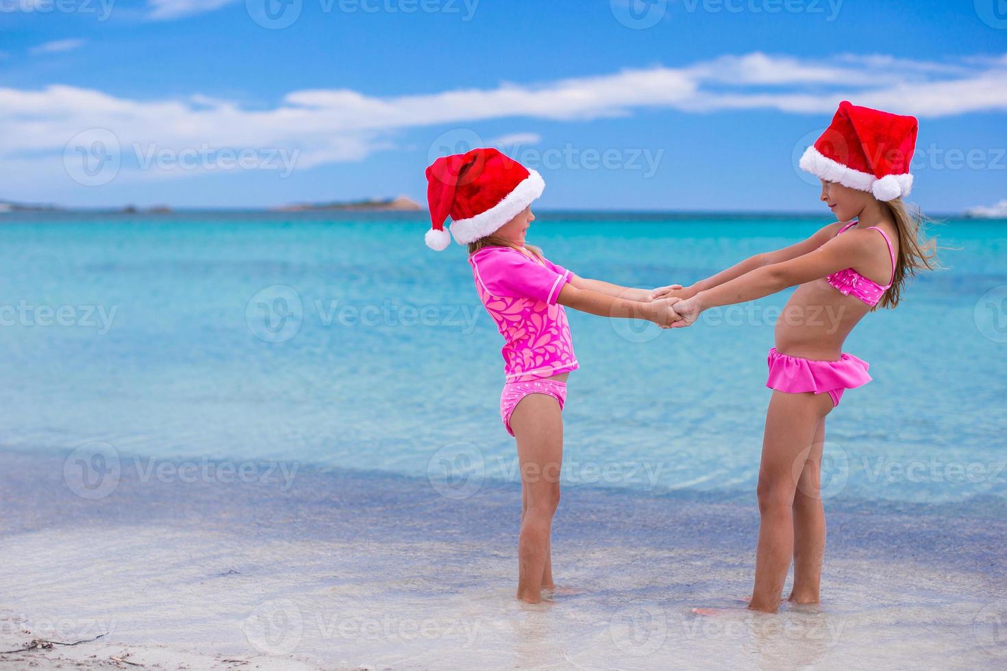 petites filles mignonnes en chapeaux de noël s'amusant sur une plage exotique photo