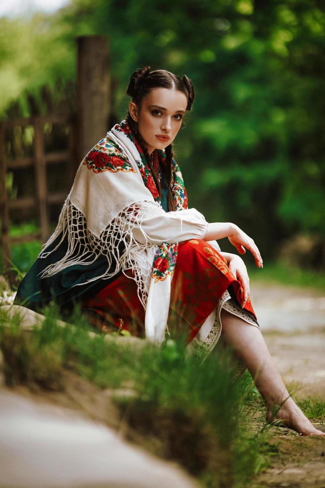 Belle jeune fille est assise dans un parc dans une robe ukrainienne colorée photo