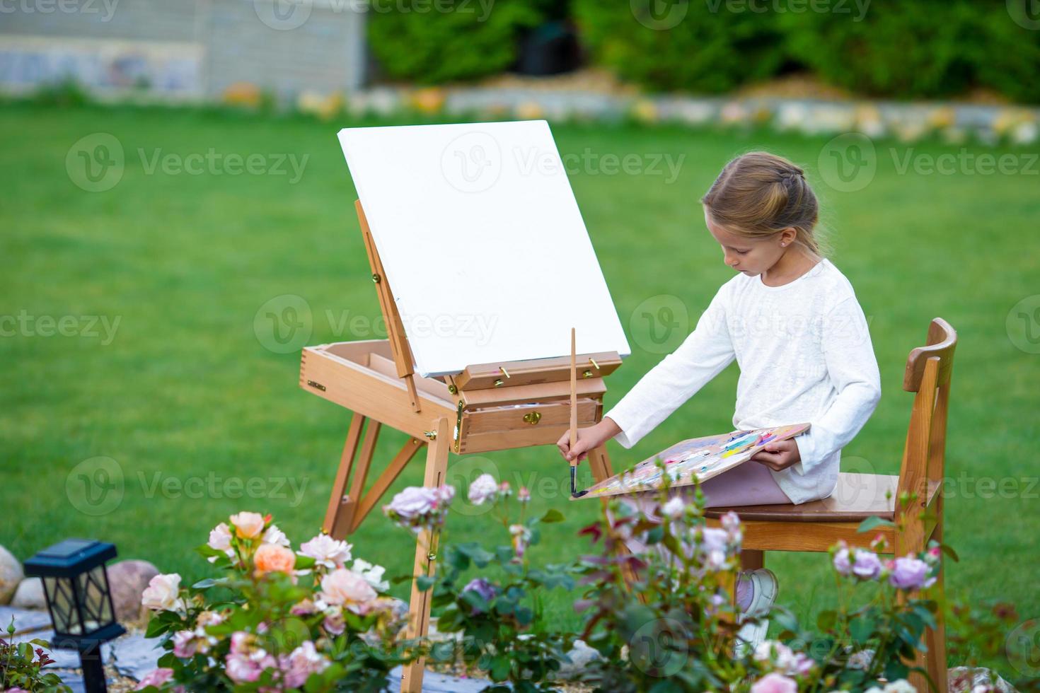 adorable petite fille peignant un tableau sur un chevalet à l'extérieur. petite artiste passionnée par son hobby. photo