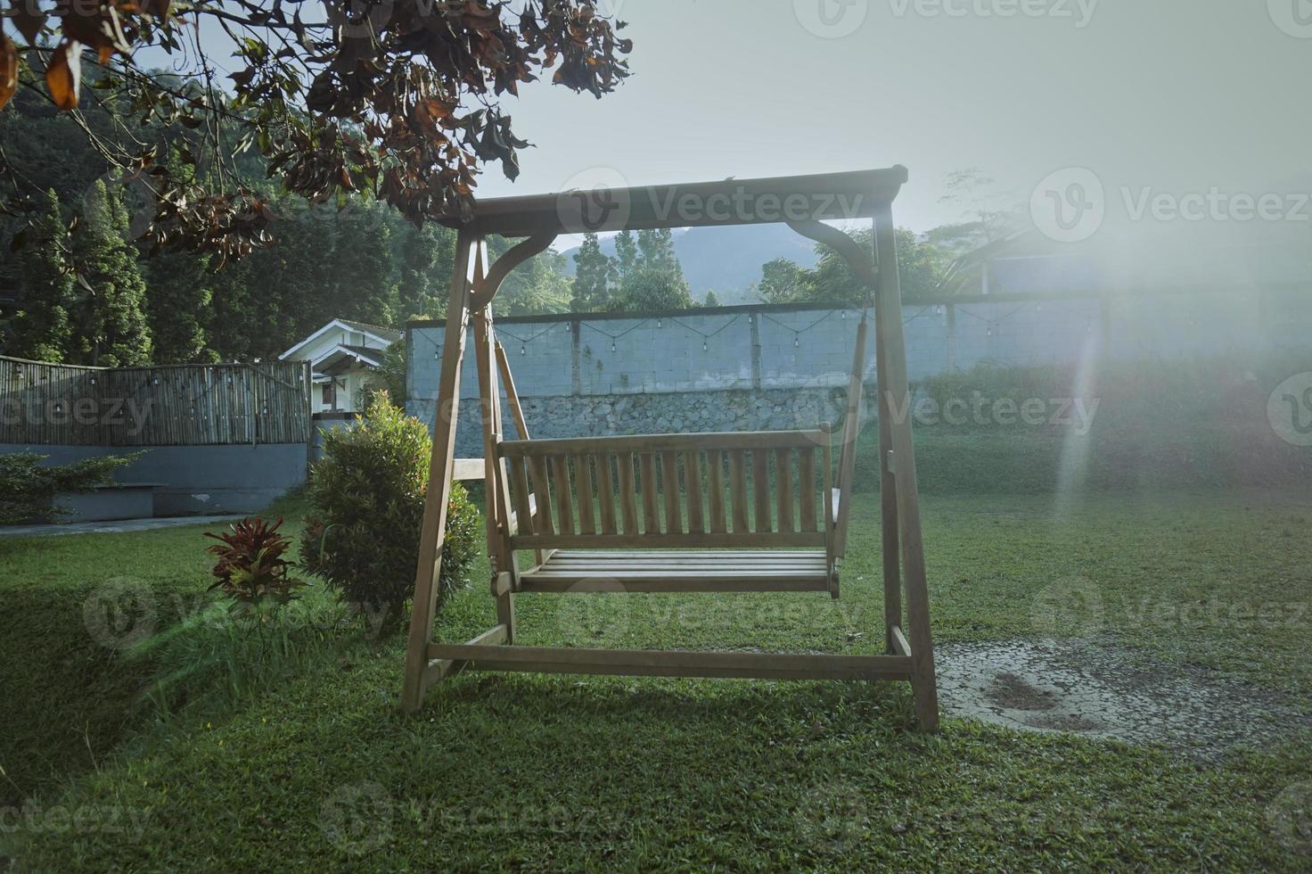 une balançoire en bois dans le jardin de la cour le matin ensoleillé avec des rayons de soleil. détendez-vous à l'air frais. meubles de jardin en bois. abstrait de la nature. photo