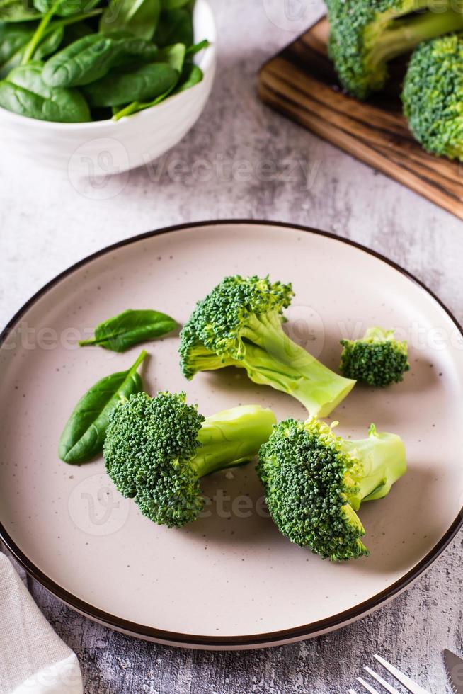 feuilles de brocoli et d'épinards frais sur une assiette sur la table. aliments sains, aliments verts. vue verticale photo