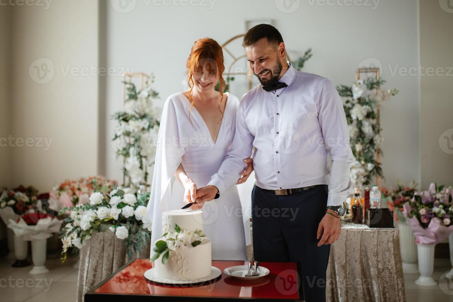 les jeunes mariés coupent et goûtent joyeusement le gâteau de mariage photo