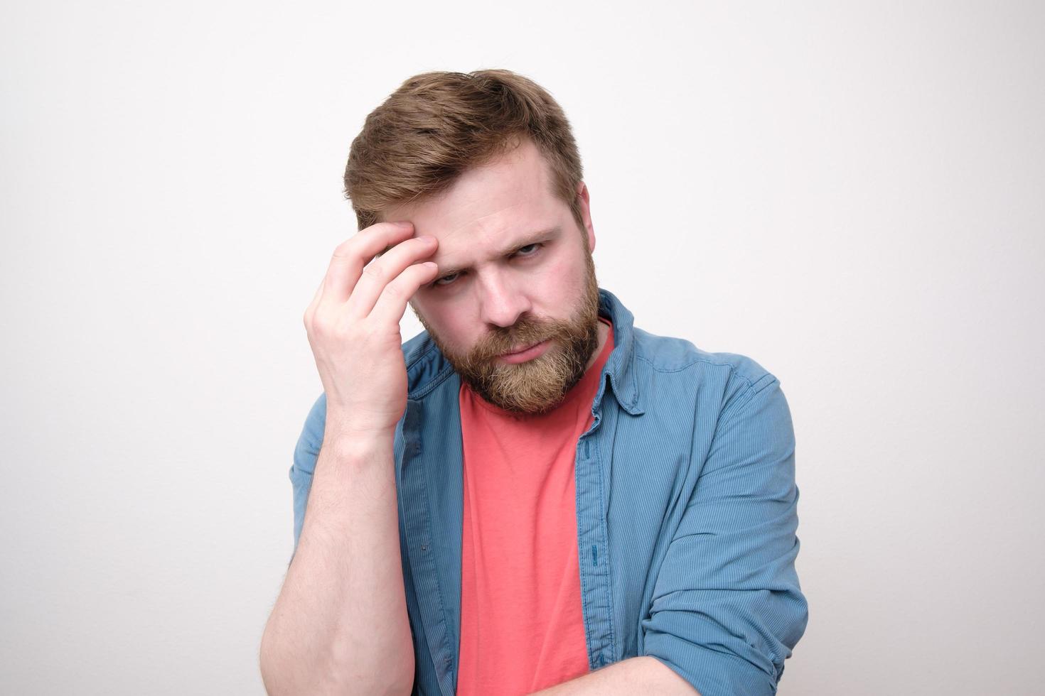 un homme caucasien mécontent tient la main sur son visage et regarde avec colère la caméra. fond blanc. photo