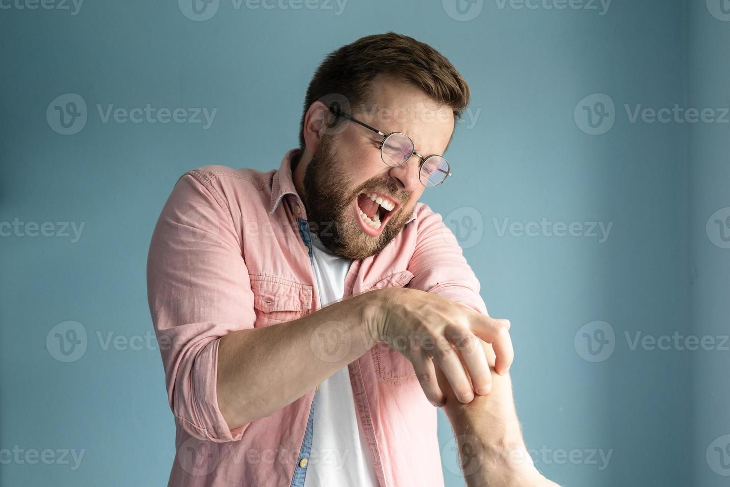 un homme malheureux et agacé gratte la peau qui démange sur le bras, ferme les yeux et crie à cause de la sensation désagréable. photo