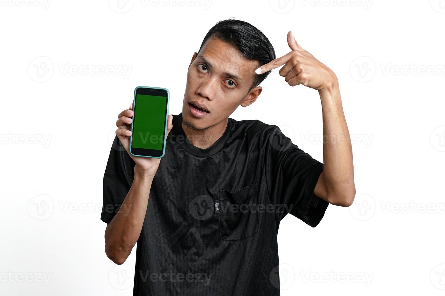 homme asiatique excité portant un t-shirt d'entraînement noir, pointant vers l'écran vert du smartphone. isolé sur fond blanc photo