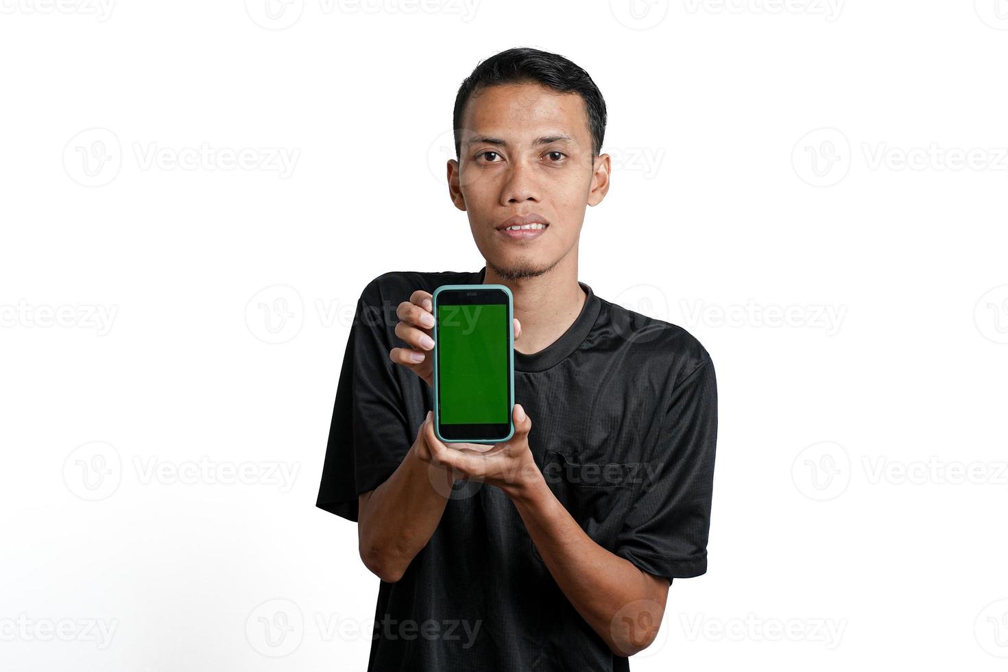 homme asiatique excité portant un t-shirt d'entraînement noir, pointant vers l'écran vert du smartphone. isolé sur fond blanc photo