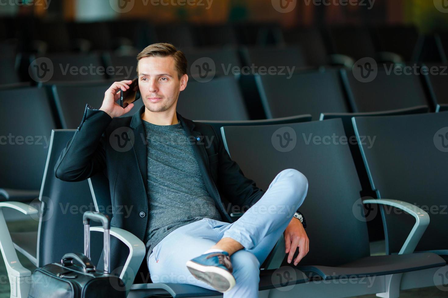 homme d'affaires urbain parlant sur un téléphone intelligent voyageant à l'intérieur de l'aéroport. jeune homme avec téléphone portable à l'aéroport en attente d'embarquement. photo