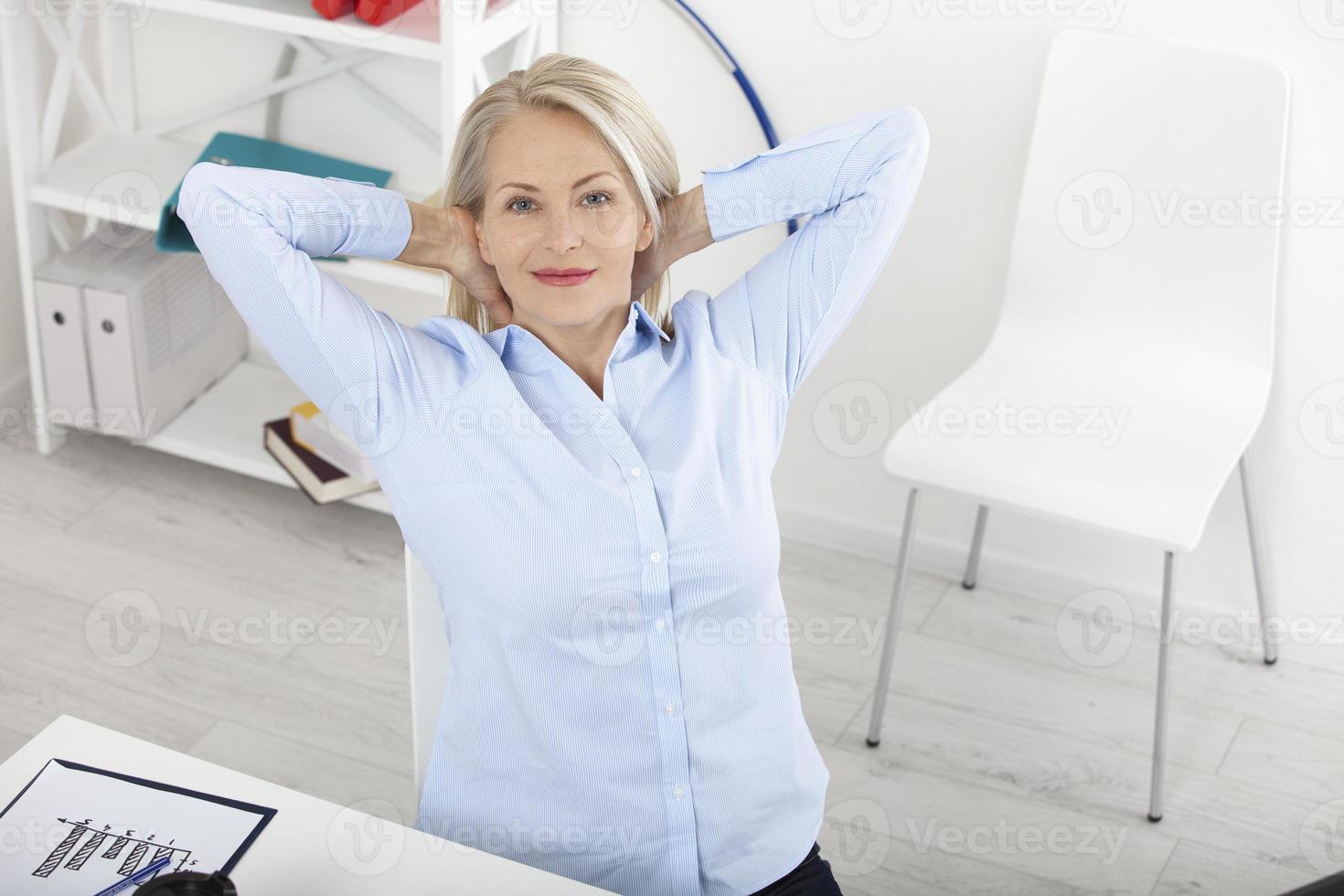 femme d'affaires moderne détendue dans les rêves. belle femme d'âge moyen regardant la caméra avec le sourire alors qu'elle était assise au bureau. photo