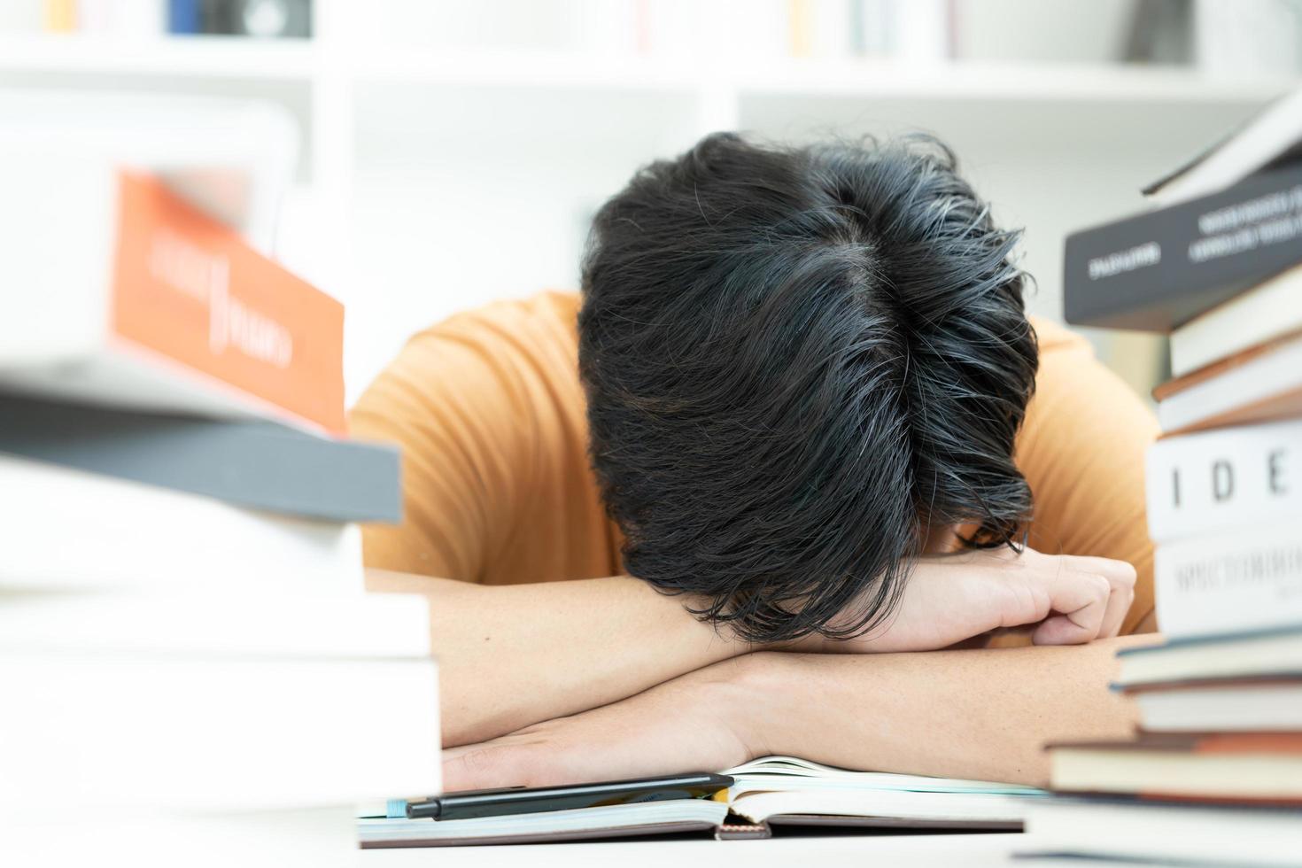 un étudiant asiatique a de l'anxiété à cause des examens, les hommes se préparent aux tests et apprennent les leçons à la bibliothèque. stress, désespoir, hâte, incompréhension lecture, découragement, attente, connaissance, fatigue photo